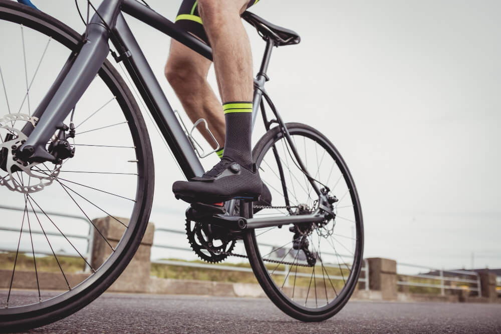 Cyclist wearing black gravel cycling shoes riding a road bike on an open road